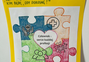 Na górze plakatu znajduje się tekst XVIII Ogólnopolski Tydzień Kariery, Szpitalne podróże w przyszłość: Kim będę jak dorosnę? Poniżej widoczne są cztery różnokolorowe puzzle, a w środku jest serce z napisem: Człowiek - serce każdej profesji. Na dole plakatu znajduje się zdanie: Każdy dzień to nowa super wiedza i krok do wymarzonego zawodu.
