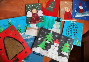 Na blacie biurka leżą rozsypane pocztówki wykonane przez dzieci dla św. Mikołaja.