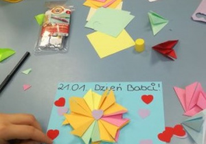 Dzieci wykonują laurki, przyklejając kwiatki wykonywane techniką origami.
