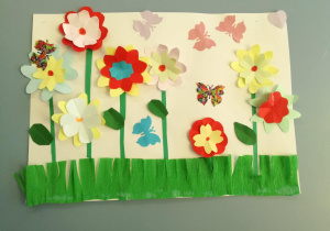 Praca plastyczna wykonana z papieru i kolorowej bibuły, przedstawiająca łąkę pełną kwiatów.