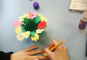 Dziecko wykonuje bukiet różnokolorowych kwiatów z kolorowego papieru.