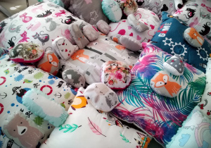 Rozłożone, kolorowe poduszki w różne wzorki: jeżyki, dziewczynki, kotki, listki, miśki i różnobarwne wzory.