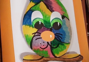 Kartka wielkanocna przedstawiająca królika w kształcie i kolorach pisanki, obok pisanek w kropki.