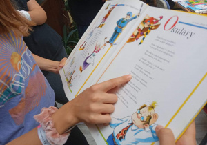 Dzieci z książką w ręku, czytają wiersz Juliana Tuwima.