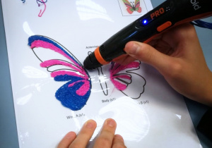 Ręce dziecka wykonującego różowo niebieskiego motyla długopisem 3D.