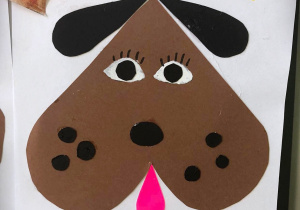 Praca plastyczna Polinki na której przyklejona jest głowa pieska w kształcie odwróconego serduszka z czarnymi uszkami i różowym języczkiem.