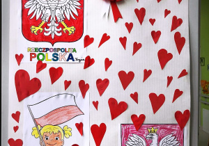 Tablica z polskimi symbolami państwowymi, na białym tle z przyklejonymi wokół serduszkami.
