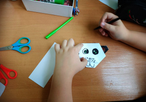 Dziecko koloruje wykonaną wcześniej przez siebie techniką origami, głowę misia pandy.