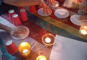 Dzieci siedzą przy stole i wróżą. Na stole stoją kubki i zapalone świece.