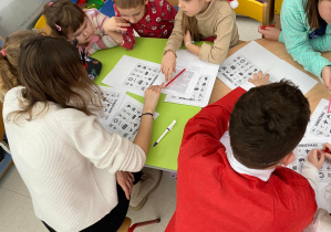 Dzieci siedzą przy stoliku z Panią i rozwiązują wspólnie zadania.