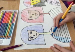 Na zdjęciu widoczne ręce dziecka rysującego pracę przedstawiającą trzy kobiety.