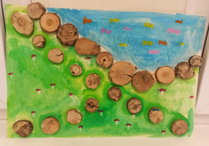 Praca plastyczna przedstawiająca trawę i wodę. Na trawie namalowane są grzyby, a w wodzie kolorowe rybki. Na środku pracy przyklejona ścieżka wykonana z okrągłych drewienek.