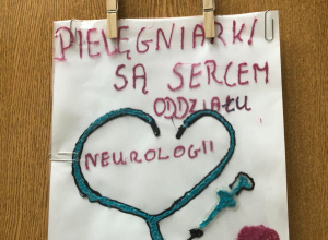 Praca plastyczna wykonana długopisem 3 D. Na białej kartce niebieski stetoskop, strzykawka i czepek oraz czerwony napis Pielęgniarki są sercem oddziału neurologii Kubuś.