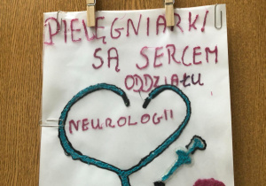 Praca plastyczna wykonana długopisem 3 D. Na białej kartce niebieski stetoskop, strzykawka i czepek oraz czerwony napis Pielęgniarki są sercem oddziału neurologii Kubuś.