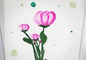 Białe tło, na nim namalowane różowe kwiaty z zielonymi łodygami. Dookoła kwiatów namalowane kropki w różnych kolorach. Na dole napis Dla Mamy.