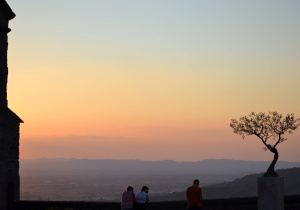 Na zdjęciu pomarańczowy zachód słońca oglądany przez ludzi stojących w punkcie widokowym.