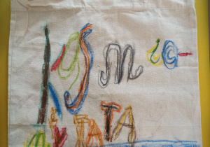 Na zdjęciu torba bawełniana pomalowana kredkami. Na obrazku kolorowy napis Kosmiczny Tata, pod nim narysowana dziewczynka z tatą.