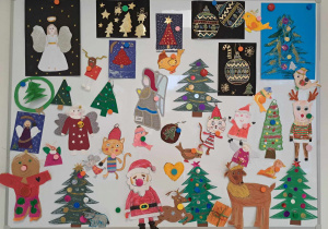 Na białej tabllicy wiszą dekoracje świąteczne. Wśród nich: Mikołaje, choinki,aniołki, bombki, piernikowe pierniczki, kotek w czapce Mikolaja.