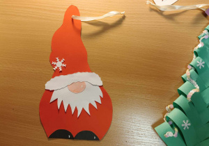 Na blacie stołu leży Mikołaj wykonany z kolorowego papieru i choinka.