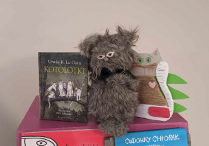 Na skrzyni owiniętej czerwoną folią siedzą dawa koty. Jeden pluszowy, drugi zrobiony z kartonu i owinięty włóczką. Obok stoi książka pod tytułem - Kotolotki.