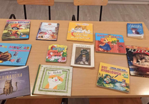 Na beżowym stole leży dwanaście książek, których bohaterami są koty. Na okładce keżej z nich też widzimy koty.