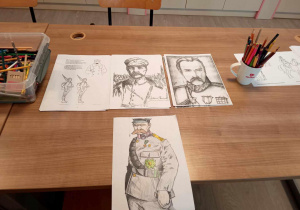 Na beżowym blacie stołu leżą kredki i kolorowanki z portretem Józefa Piłsudskiego oraz jego wojska.