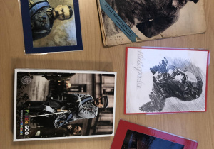 Na blacie beżowego stołu leżą 4 zdjęcia i jeden szkic portretu Józefa Piłsudskiego