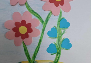 W malowanym żółtym wazonie doklejono różowo-czerwone kwiaty