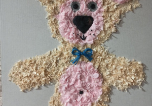 Ręcznie wykonany miś z bibuły w jasnych i różowych kolorach, ozdobiony niebieską kokardką.