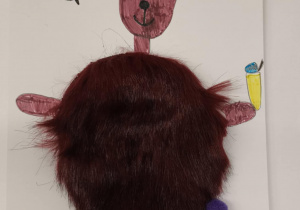 Kolorowa praca plastyczna przedstawiająca misia z futrzanym brzuchem na tle rysunku z pszczółkami, słońcem i trawą.