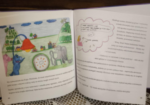 Na ilustracji widać fantastyczny świat kucyków — kolorowe, baśniowe stworzenia pracują przy wielkiej czerwonej lampie i ognisku, otoczone zielonymi wzgórzami i domkami. Obok znajduje się fragment opowieści o Grey, która po trudnej podróży ratuje dolinę, a mieszkańcy witają ją z radością i wdzięcznością, odkrywając, że ma prawdziwe skrzydła.