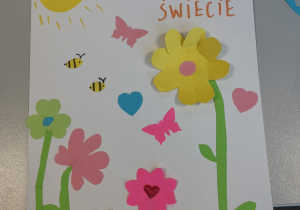 Laurka dla mamy z napisem „Dla najlepszej mamy na świecie”, ozdobiona kolorowymi kwiatami, słońcem, serduszkami i motylkami.