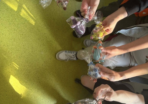 Zdjęcie przedstawia ręce uczniów które tworzą półokrąg. W dłoni każdy trzyma wykonaną szydełkiem myszkę-prezenty otrzymane z okazji Dnia Dziecka.