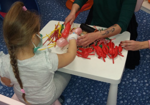 Pani z dziewczynką siedzą przy stoliku i wiąża balonik