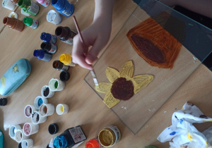 Ręka dziecka malującego obrazek ze słonecznikiem w doniczce