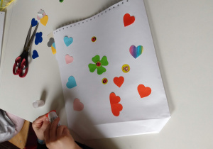 Dziecko na białej kartce nakleja kolorowe serduszka