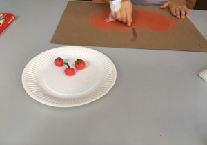 jabłka wykonane z plasteliny na papierowym talerzyku i dziecko rysujące jabłko