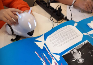 Dziecko bawiące się robotem ze świecącymi oczami przy niebieskim kartonie z plakatem dotyczącym Stanisława Lema