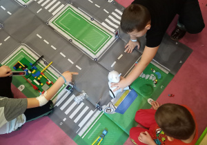 Dzieci siedzą przy makiecie przedstawiającej skrzyżowania dróg i bawią się Photonem.